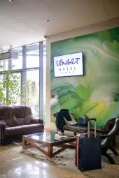 Recepcja hotelu z zieloną ścianą, sofą, stolikiem i walizką.