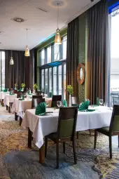 Elegancka restauracja z białymi obrusami, zielonymi dekoracjami i dużymi oknami.