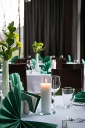Elegancko nakryty stół w restauracji z zielonymi dekoracjami i świecą.