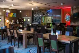 Nowoczesna restauracja z drewnianymi stołami, zielonymi krzesłami i nastrojowym oświetleniem.
