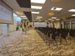 Pusta sala konferencyjna z rzędem krzeseł i ekranem projekcyjnym.