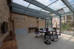Nowoczesne wnętrze z przeszklonym dachem, drewnianym stołem i kamienną ścianą.