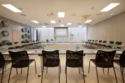 Nowoczesna sala konferencyjna z ustawionymi krzesłami i stołem, ekranem oraz flipchartem.