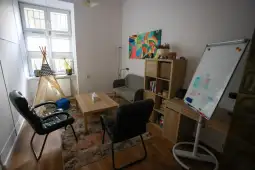 Nowoczesne biuro z meblami, roślinami i kolorowym obrazem na ścianie.