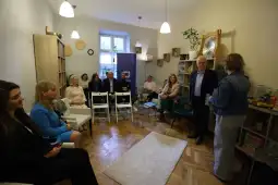 Spotkanie grupy ludzi w przytulnym wnętrzu z regałami i dekoracjami.