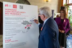 Mężczyzna podpisuje manifest kampanii wspierającej dzieciństwo bez przemocy. W tle kobieta obserwuje.