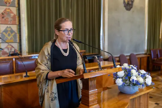 Kobieta przemawia przy mównicy, obok bukiet kwiatów.