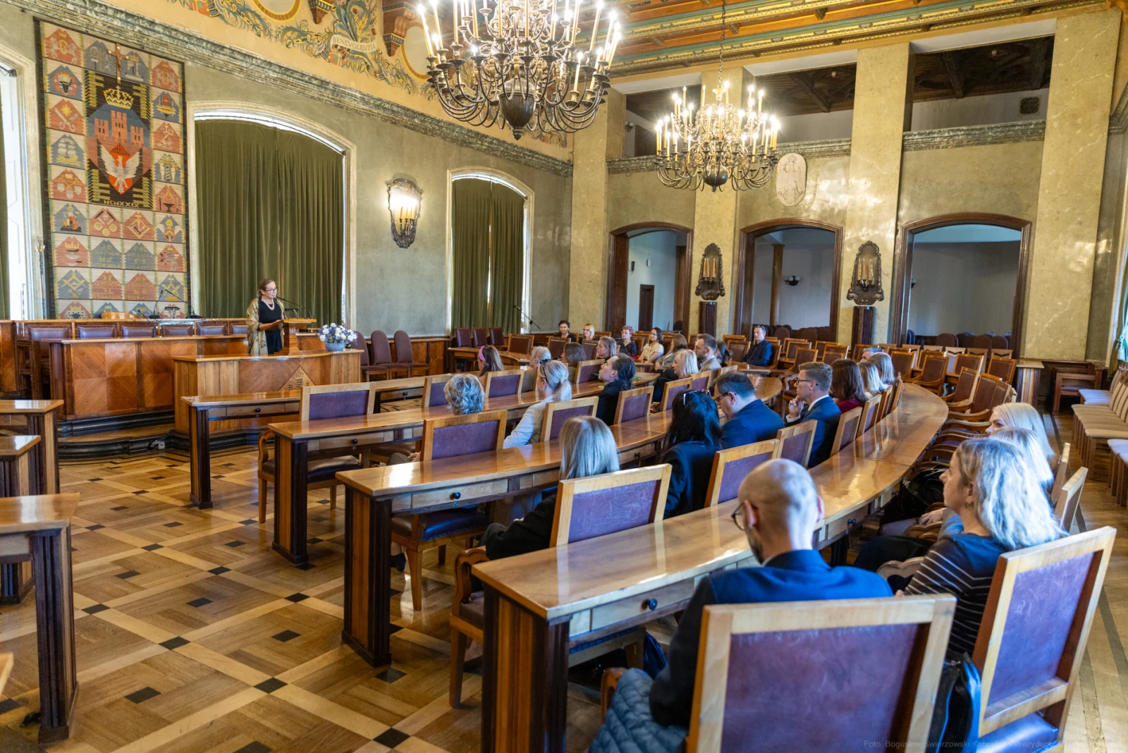 Spotkanie w sali z drewnianymi ławami i żyrandolami, uczestnicy słuchają prelegenta.  Autor: Bogusław Świerzowski