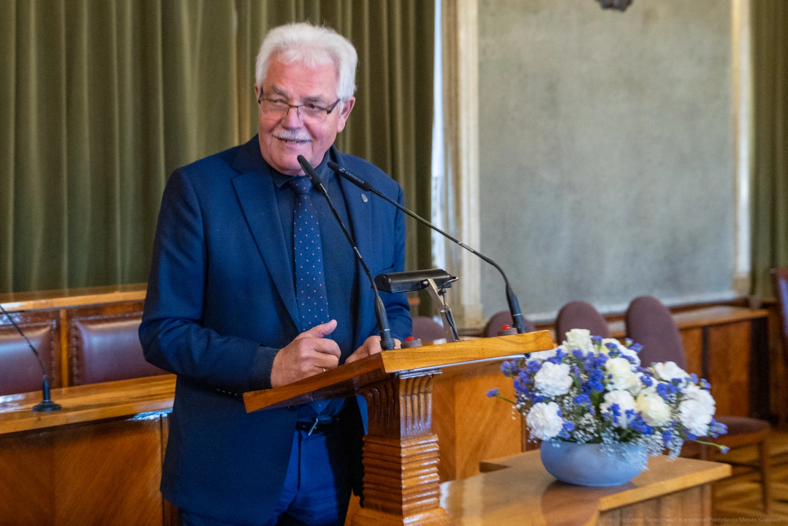Mężczyzna w garniturze przemawia przy mównicy, obok bukiet kwiatów.  Autor: Bogusław Świerzowski