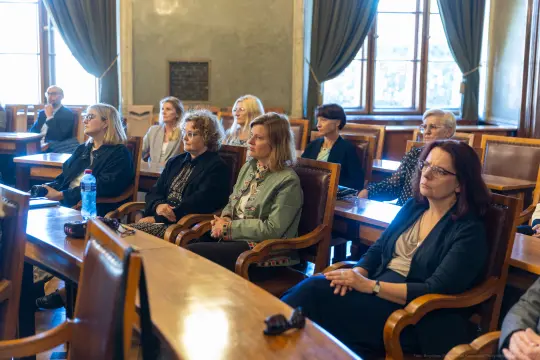 Grupa osób siedzących w sali konferencyjnej, skupionych na prelekcji.