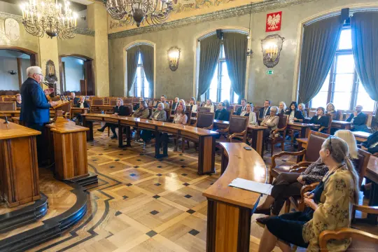 Spotkanie w sali obrad z uczestnikami siedzącymi w rzędach.