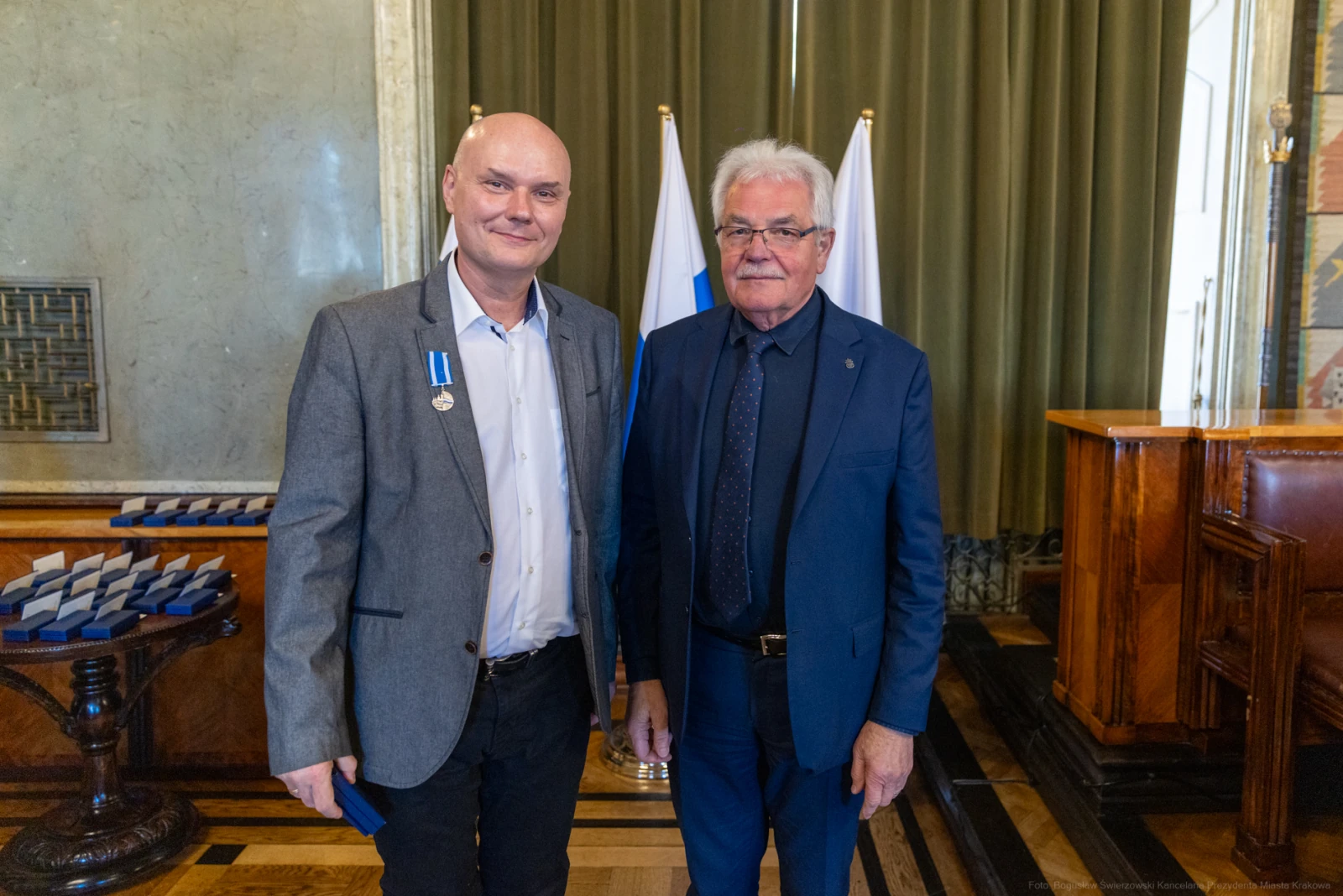 Dwaj mężczyźni w garniturach, jeden z medalem, stoją w eleganckim wnętrzu.  Autor: Bogusław Świerzowski