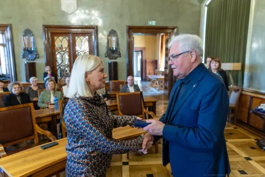 Wręczenie nagrody w sali konferencyjnej, uściski dłoni między dwiema osobami.