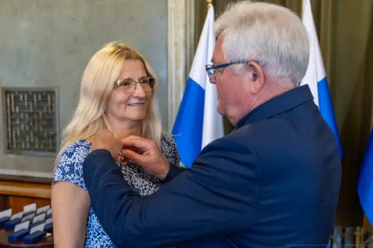 Wręczenie odznaczenia kobiecie przez mężczyznę w formalnym otoczeniu.