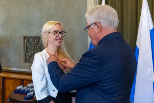Wręczenie odznaczenia kobiecie przez mężczyznę w formalnym otoczeniu.
