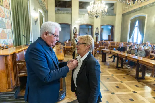 Uroczystość wręczenia odznaczenia w sali obrad z obecnymi gośćmi.