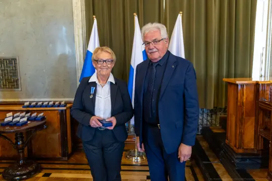 Wręczenie odznaczenia w uroczystej atmosferze, dwie osoby w formalnych strojach.
