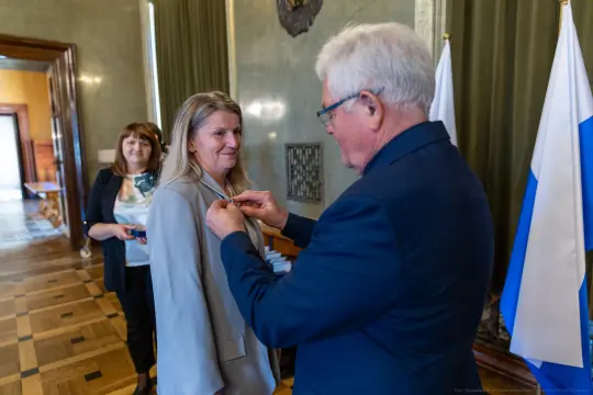 Wręczenie odznaczenia kobiecie przez mężczyznę w formalnym otoczeniu.