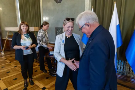 Uroczystość wręczenia odznaczeń, uśmiechnięte osoby w formalnych strojach.
