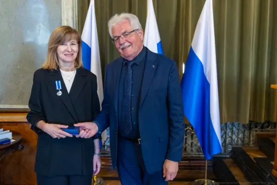 Wręczenie odznaczenia przez mężczyznę kobiecie w towarzystwie flag.
