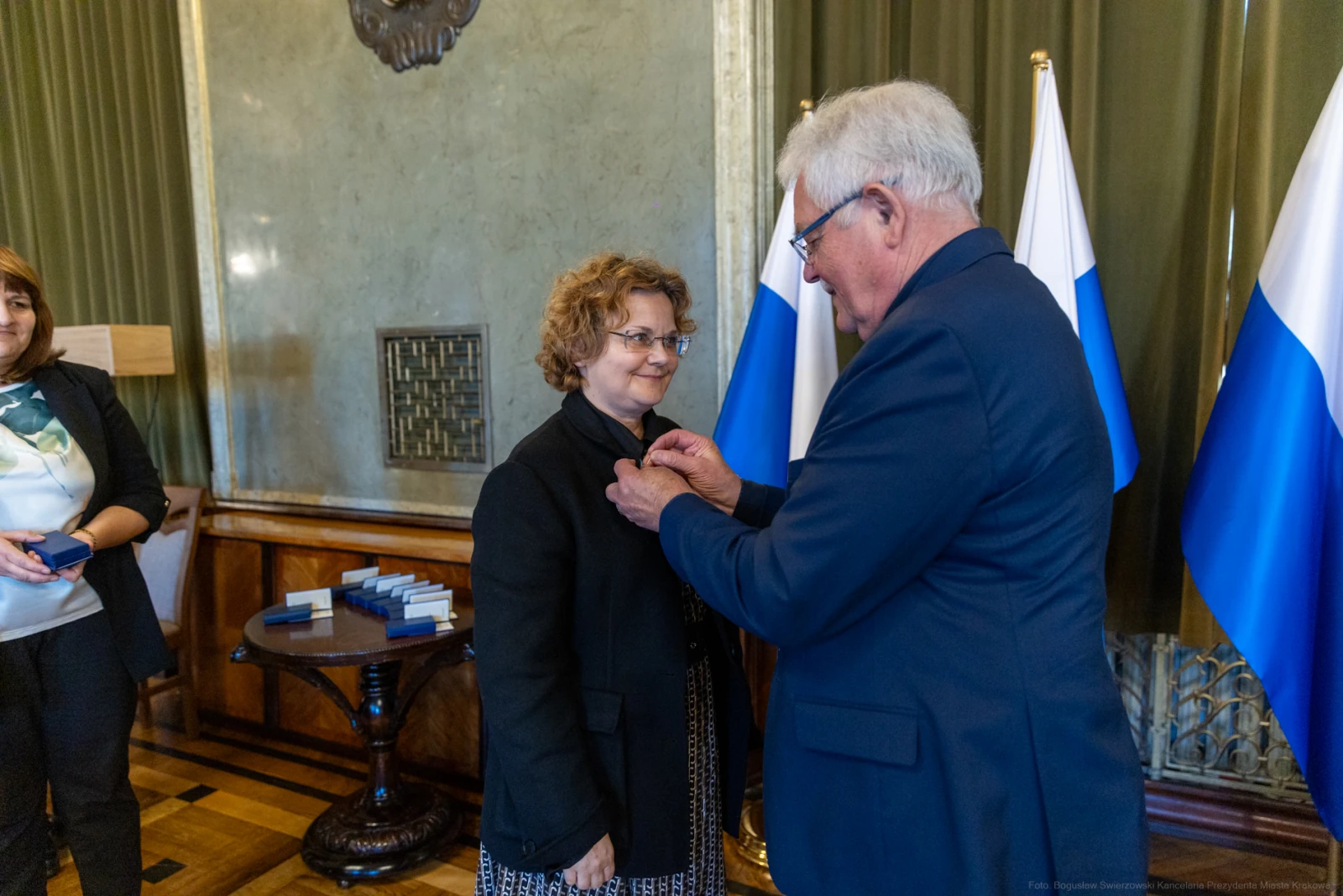 Wręczenie odznaczenia przez mężczyznę kobiecie w eleganckim wnętrzu.  Autor: Bogusław Świerzowski