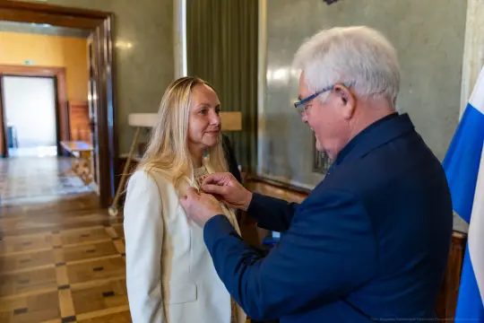 Mężczyzna przypina odznaczenie do marynarki kobiety w eleganckim wnętrzu.