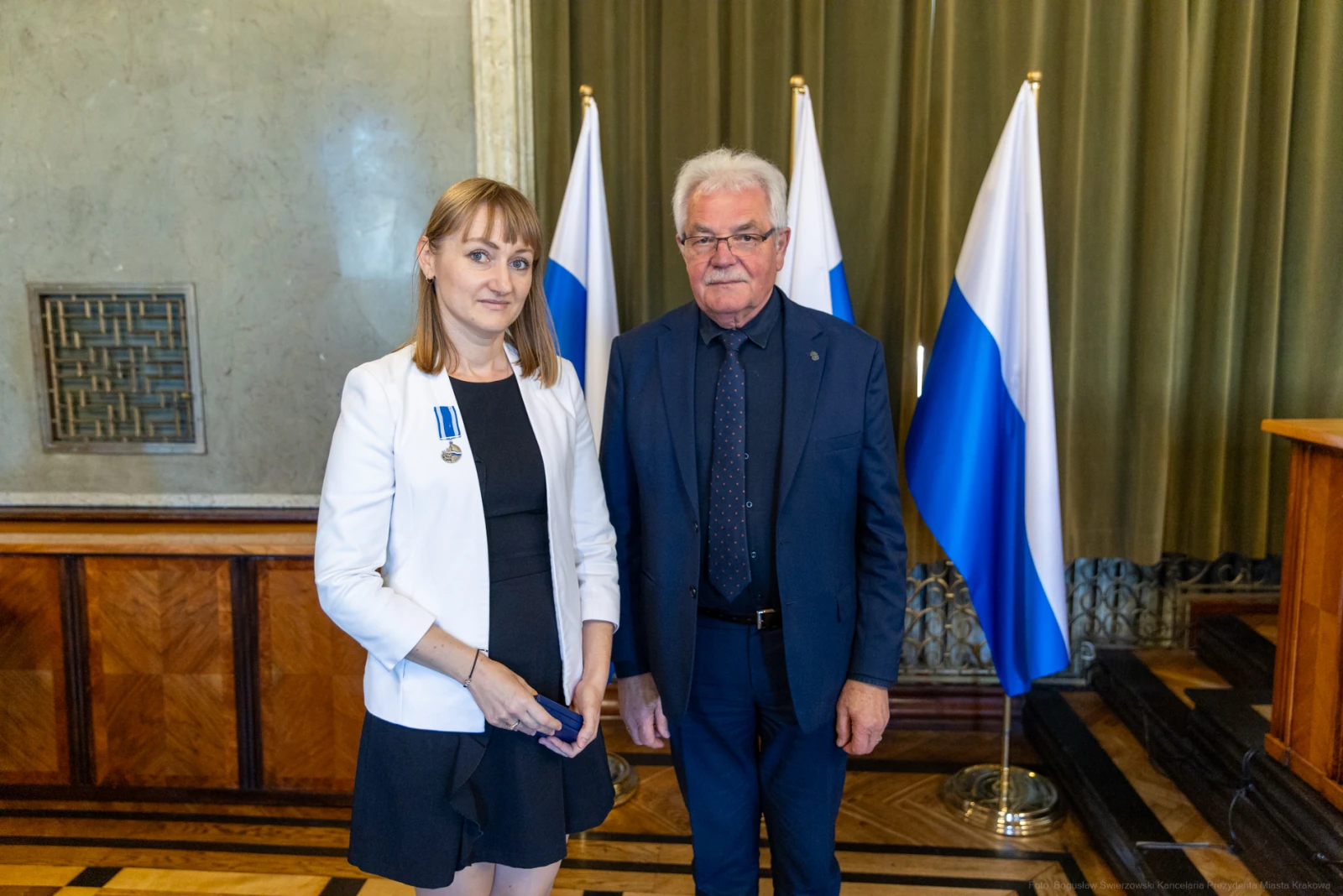 Wręczenie odznaczeń w obecności flagi. Dwoje ludzi w formalnych strojach.  Autor: Bogusław Świerzowski