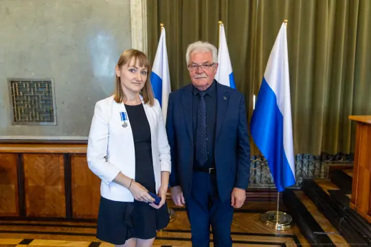 Wręczenie odznaczeń w obecności flagi. Dwoje ludzi w formalnych strojach.