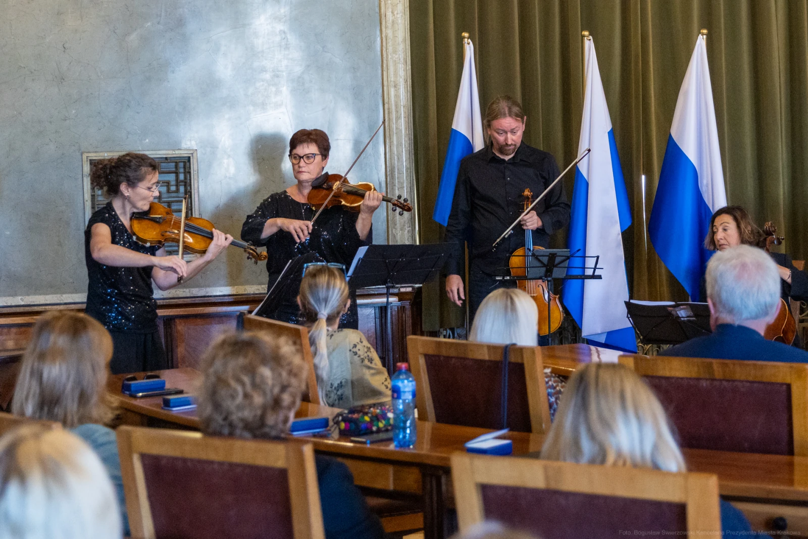 Muzycy grający na skrzypcach podczas koncertu w sali z flagami.  Autor: Bogusław Świerzowski
