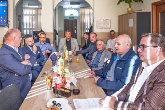 Grupa mężczyzn w sali konferencyjnej, rozmawiających przy stole z napojami i przekąskami.