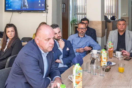 Grupa ludzi siedzących przy stole, uczestniczących w spotkaniu.