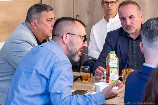 Mężczyźni w rozmowie przy stole, na stole napój i przekąski.