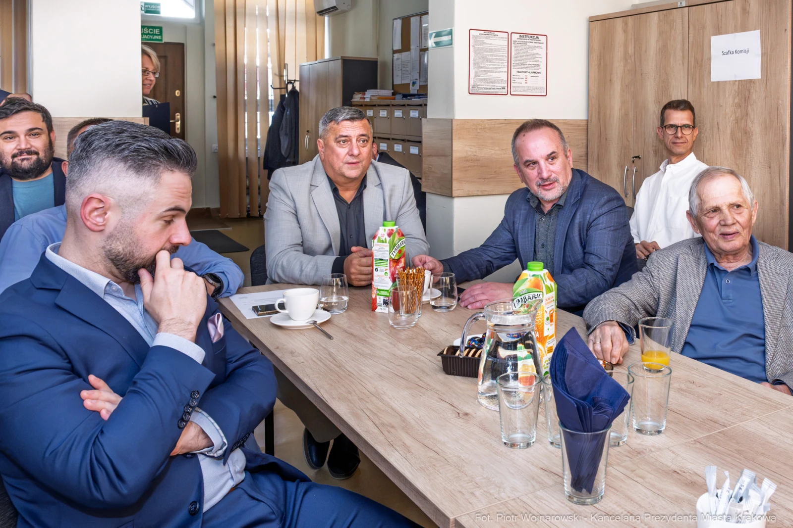 Grupa mężczyzn siedzących przy stole w kawiarni, rozmawiających i pijących napoje.  Autor: Piotr Wojnarowski