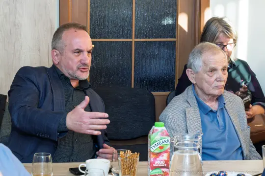 Mężczyźni rozmawiają przy stole, na stole napój i filiżanki.