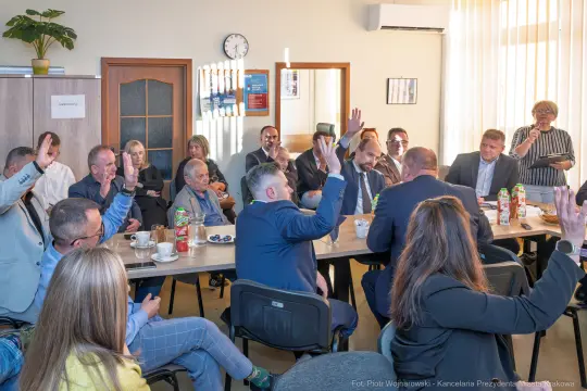 Spotkanie grupy ludzi w sali konferencyjnej, podnoszą ręce w głosowaniu.