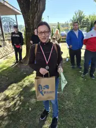 Kobieta z medalem i torbą na tle grupy ludzi w parku.