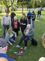 Grupa osób uczestniczy w aktywności na świeżym powietrzu, w tym starsze panie i młodsze osoby.