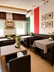 Wnętrze restauracji z brązowymi stołami i krzesłami, w tle zielona i czerwona ściana.