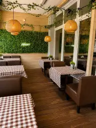 Stylowa restauracja z brązowymi stołami i lampami, otoczona zielonymi roślinami.