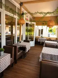 Przytulna restauracja z brązowymi stołami i krzesłami, ozdobiona roślinami i lampionami.