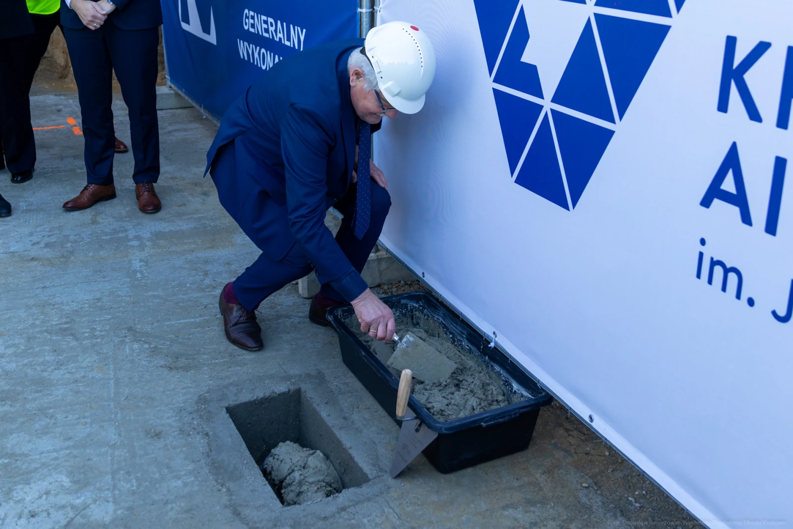 Osoba w kasku wylewa beton w wykopie, obok baner z logo inwestycji.  Autor: Bogusław Świerzowski
