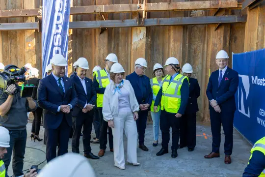 Grupa osób w kaskach budowlanych na placu budowy.