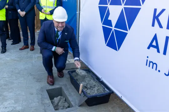 Mężczyzna w kasku budowlanym przygotowuje zaprawę w miejscu budowy.