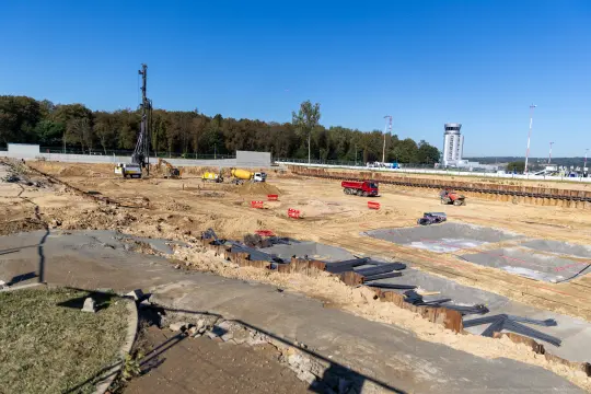 Plac budowy z maszynami, wykopami i materiałami budowlanymi.