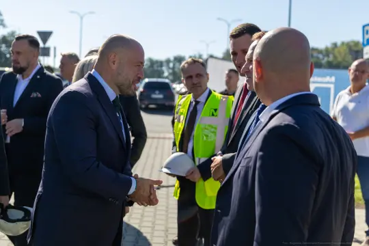 Spotkanie mężczyzn w garniturach, rozmowa przy budowie, obecność pracowników w kamizelkach.