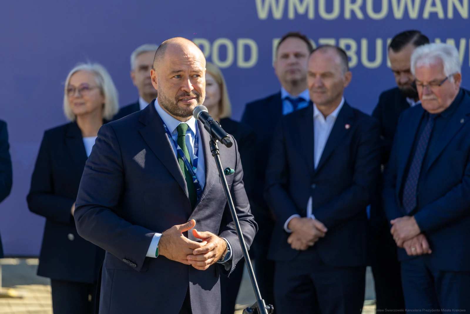 Mężczyzna przemawia do mikrofonu, w tle grupa osób w garniturach.  Autor: Bogusław Świerzowski