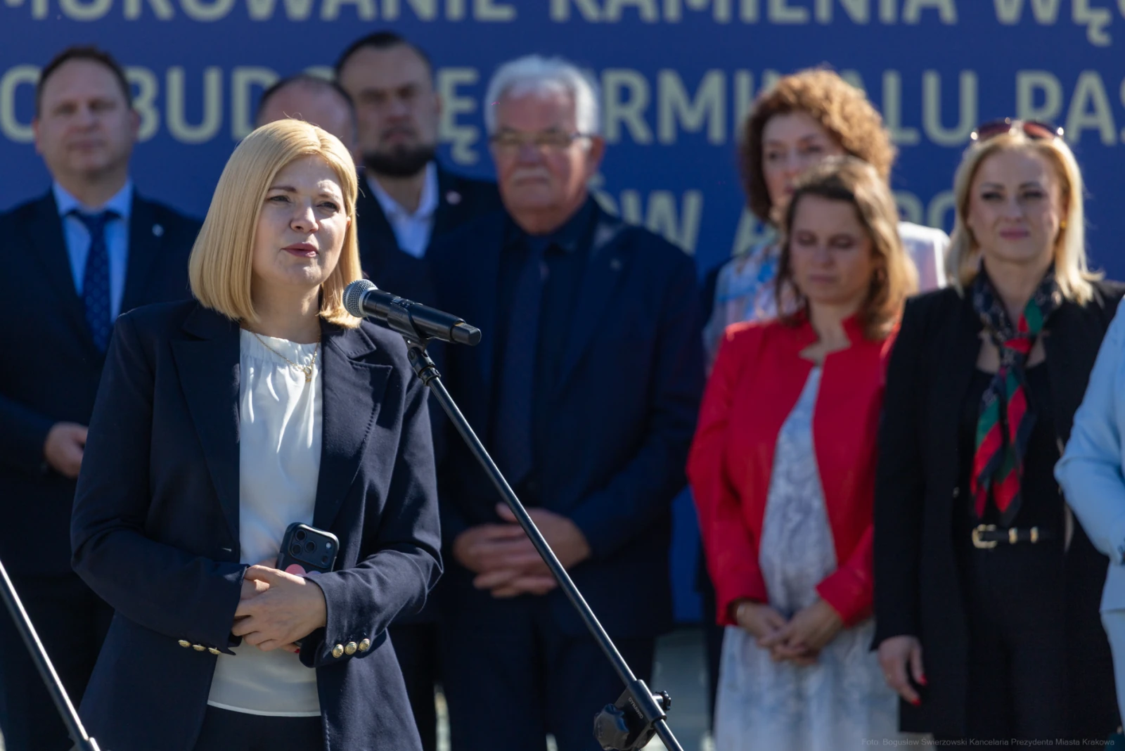 Kobieta przemawia do mikrofonu, w tle grupa osób w formalnych strojach.  Autor: Bogusław Świerzowski
