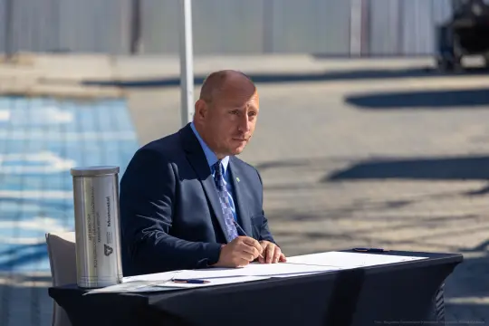 Mężczyzna w garniturze siedzi przy stole, pisząc na kartce.
