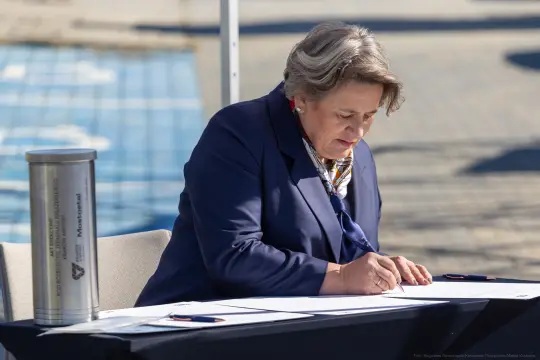 Kobieta w garniturze podpisuje dokumenty przy stole.