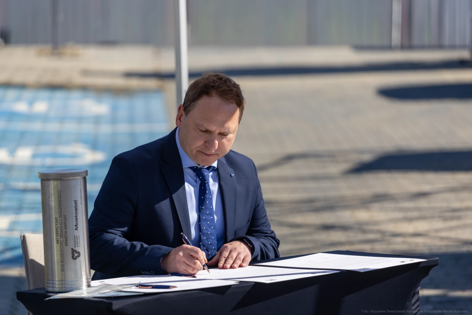Mężczyzna w garniturze podpisuje dokumenty przy stole.  Autor: Bogusław Świerzowski
